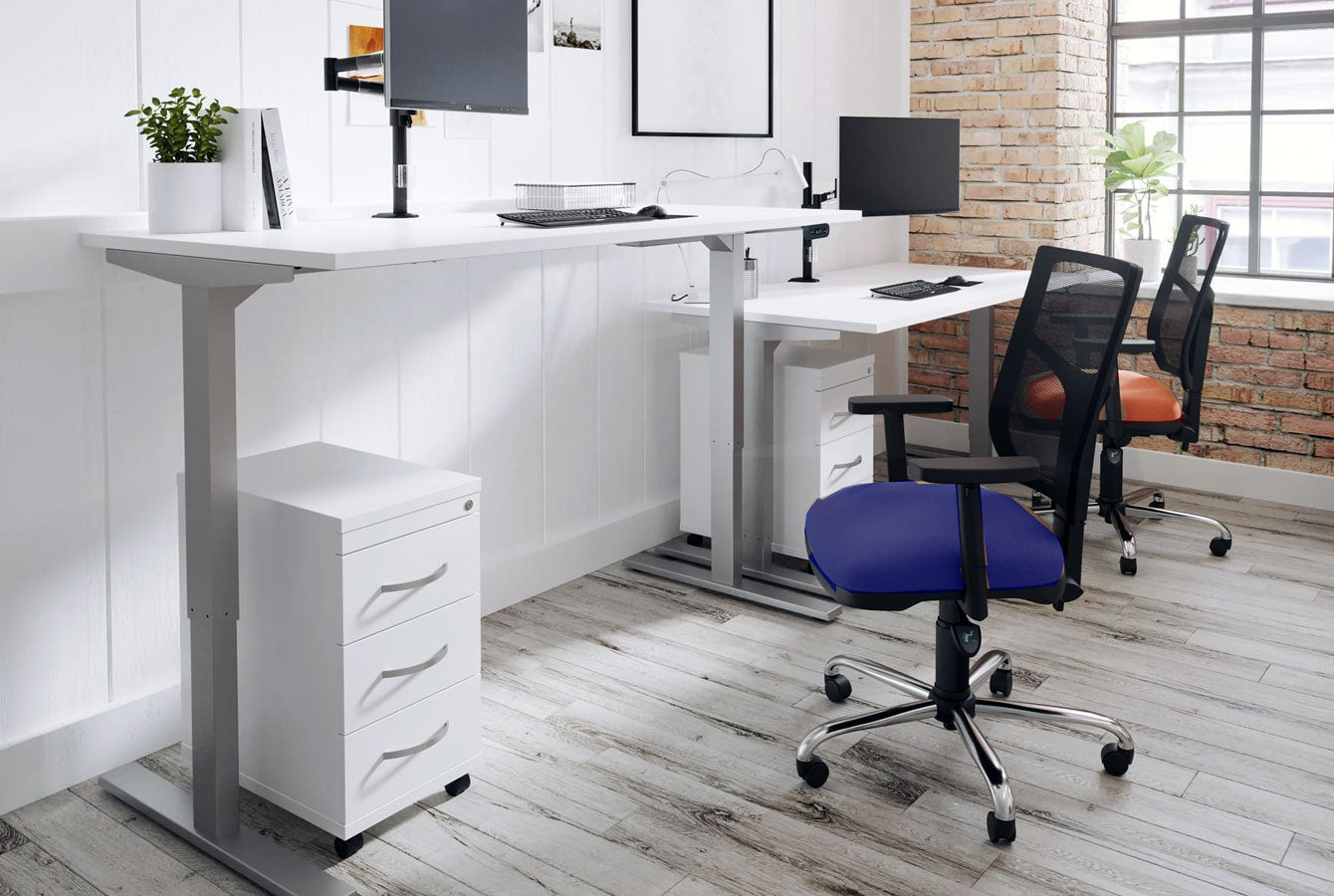 Modern office setup with adjustable desks, chairs, and a filing cabinet.