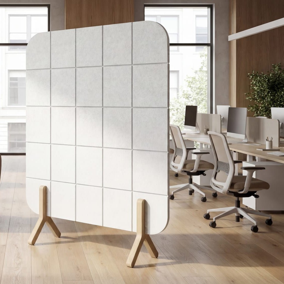 A modern white panel room divider with a grid pattern and wooden legs, shown in a bright, contemporary office lounge setting.
