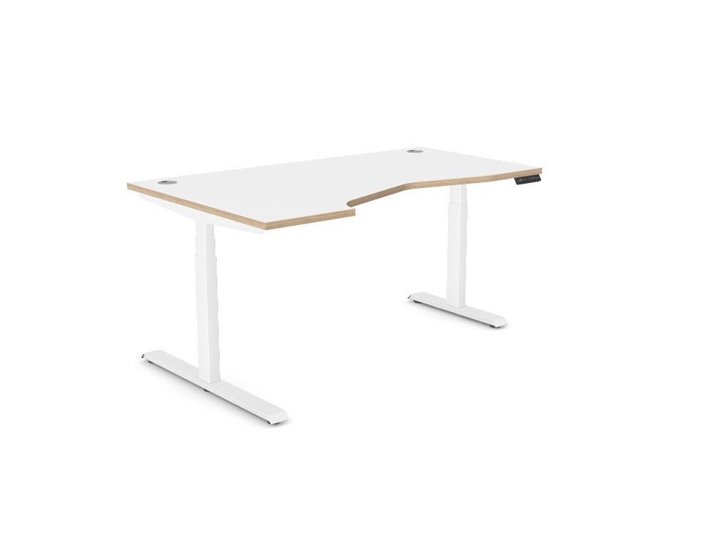 An L-shaped standing desk with a white top and light wood grain edges, supported by a white metal T-style base, shown on a solid white background.
