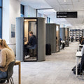 A modern library interior with students studying in private soundproof pods and at shared desks. Tall bookshelves line the back wall, and a ceiling sign indicates Group Study and Silent Study.