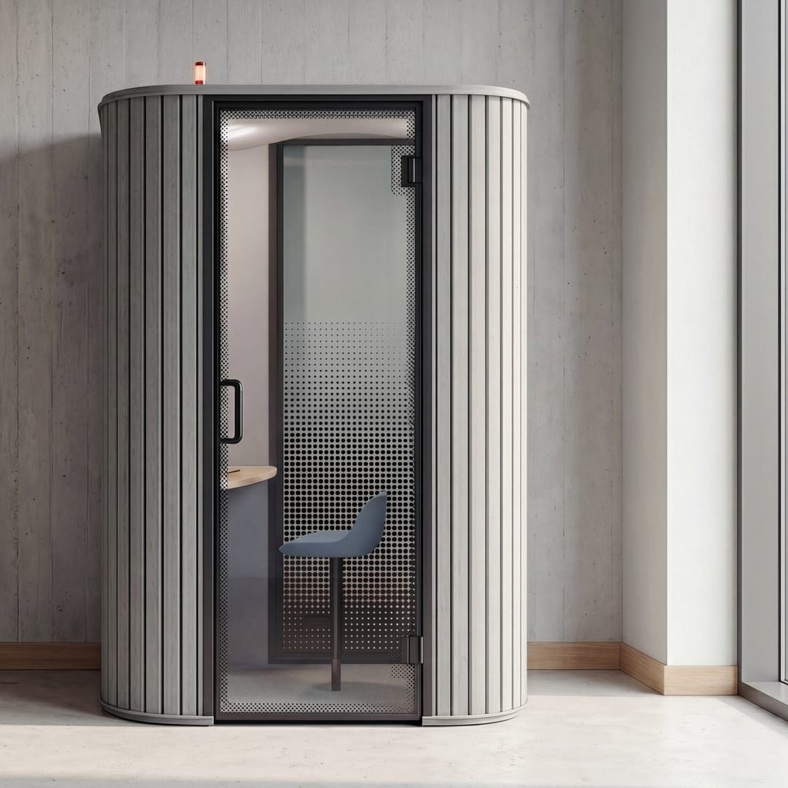 A modern cylindrical indoor sauna or privacy room with a ribbed gray exterior, black-framed glass door, and visible interior seating, shown in a minimalist interior setting.
