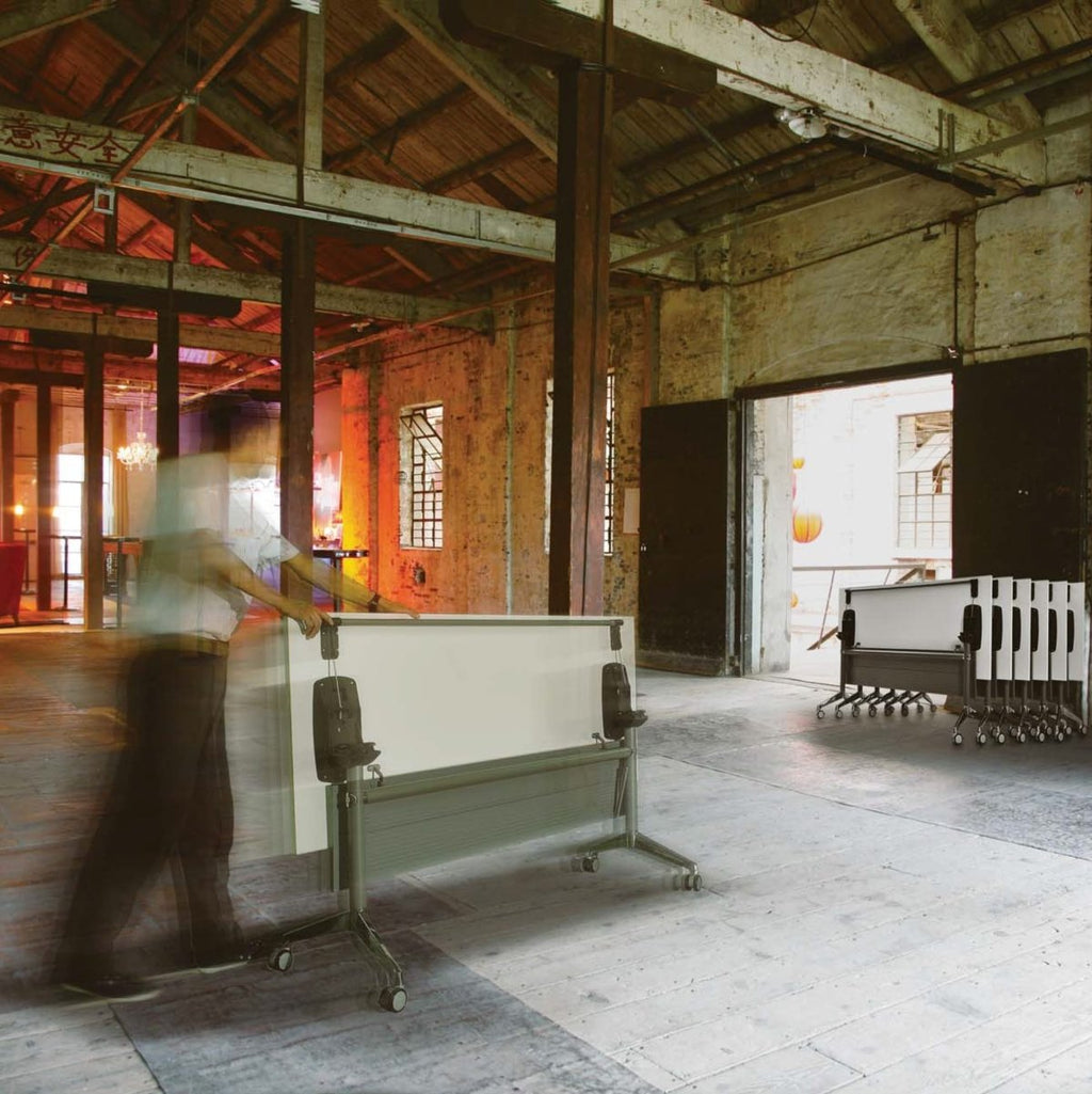Large room with high ceilings and wooden beams, featuring a whiteboard on wheels.