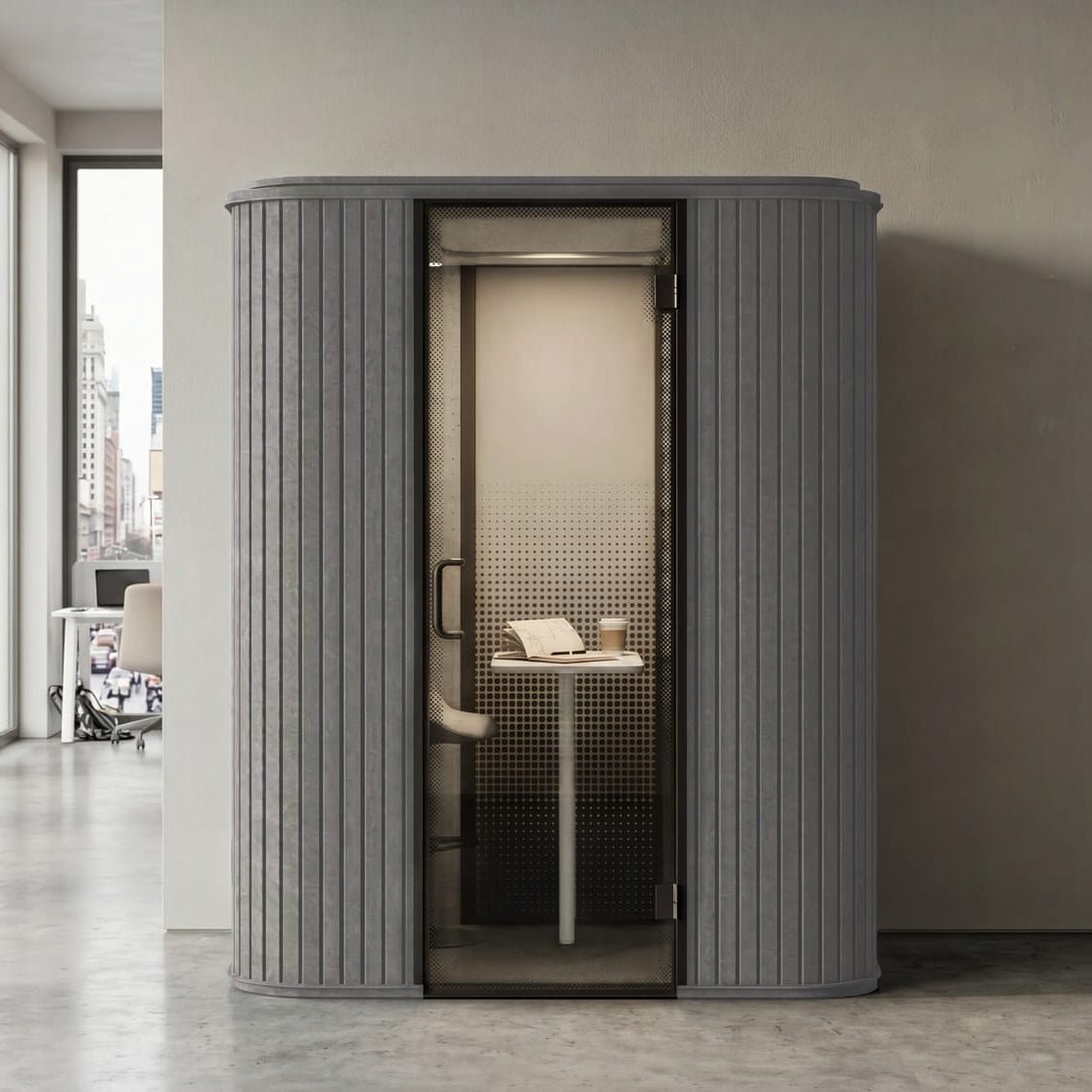 A modern gray privacy pod phone booth with a glass door, set against a minimalist beige wall in an office hallway.