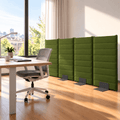 A set of four green upholstered office partition panels with dark metal feet, arranged in a modern office space next to a desk and chair.