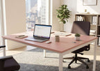 Modern office desk with laptop, chairs, and decor in a bright room with large windows.