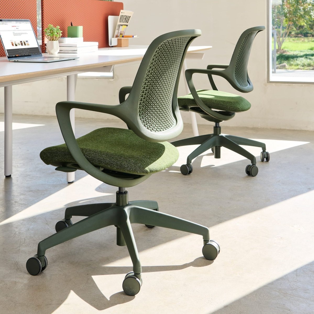 Green office chairs in a modern office setting with large windows.