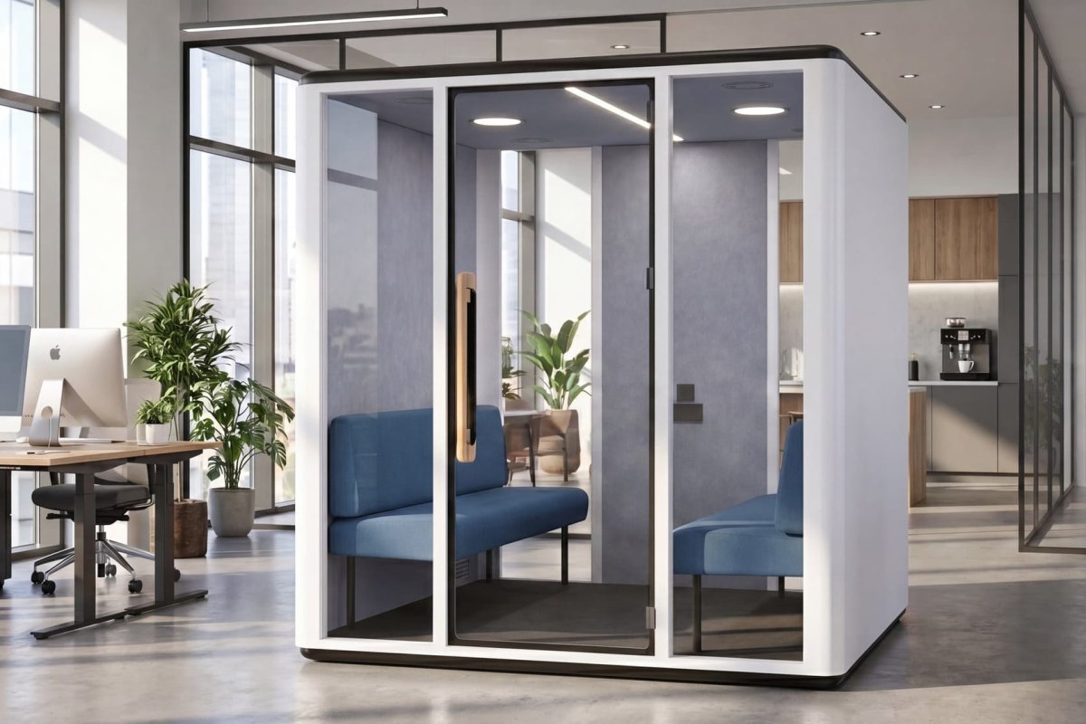 A modern glass-walled private office cubicle with blue upholstered seating inside, shown in a bright contemporary office space with desks, chairs, and plants.
