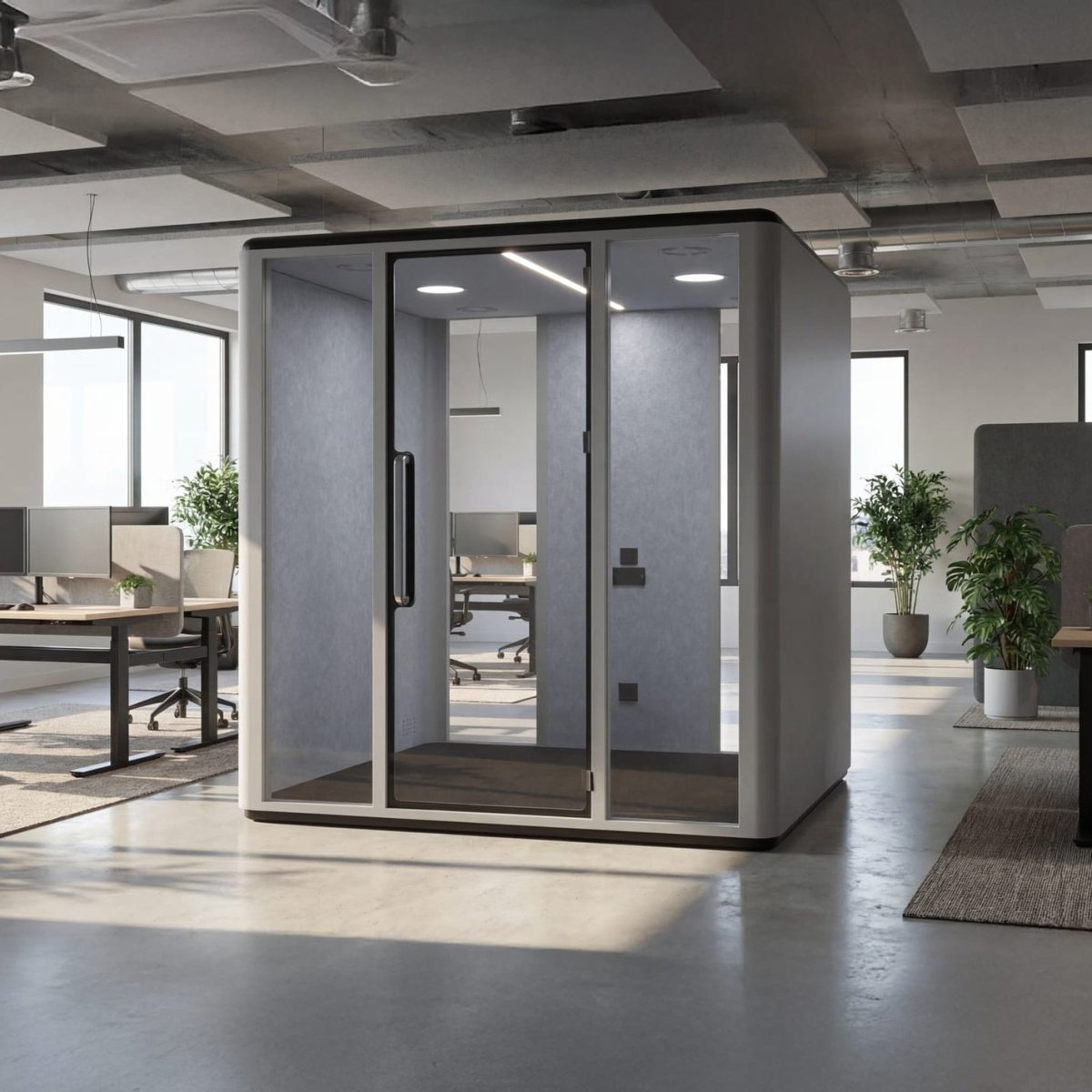 A modern glass and panel privacy booth with a gray exterior and black frame, situated in a bright, contemporary open-plan office.